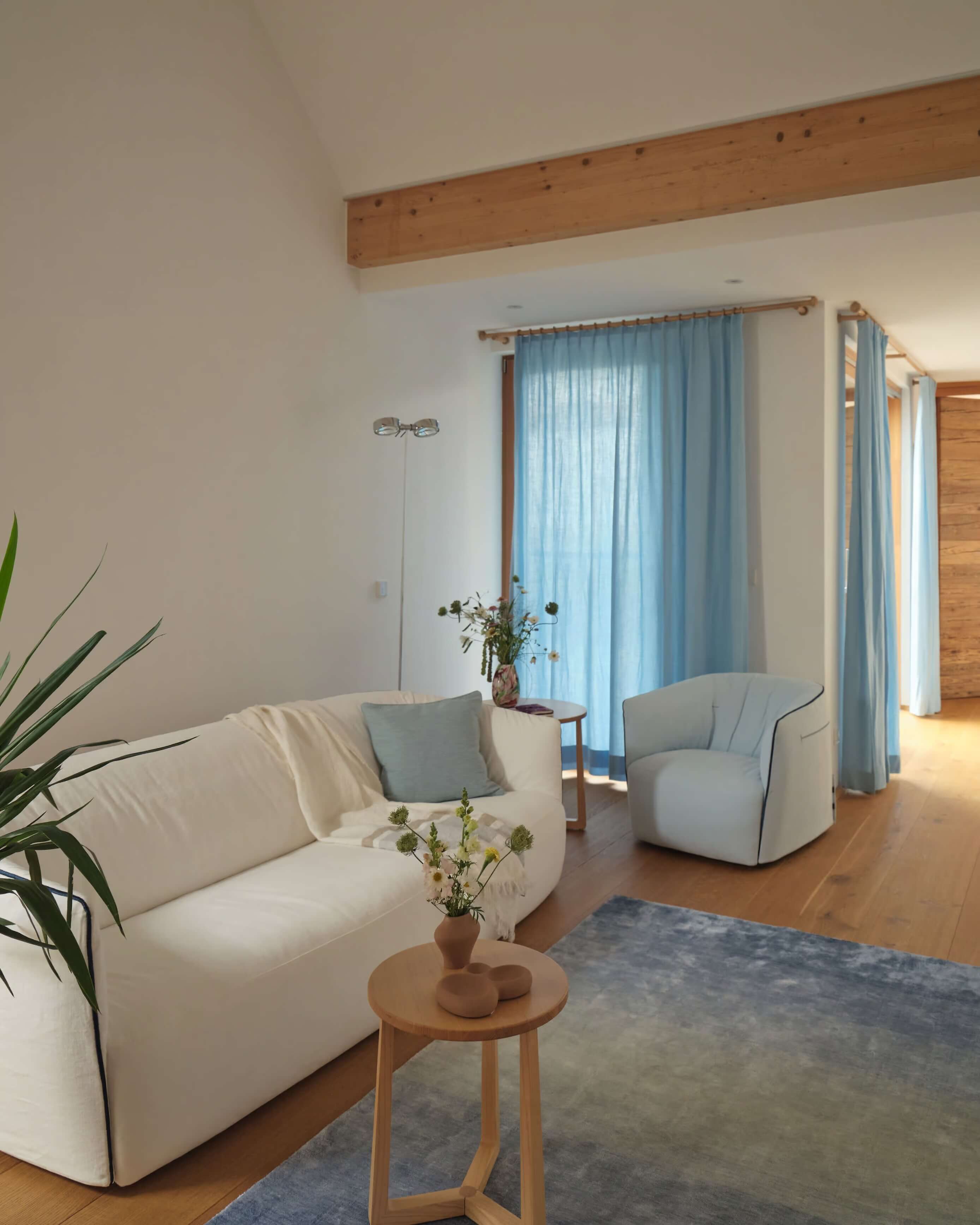 Sunlit living area in an attic suite at JK7® Spa Wellnes with blue curtains, a white sofa, and a light blue armchair.